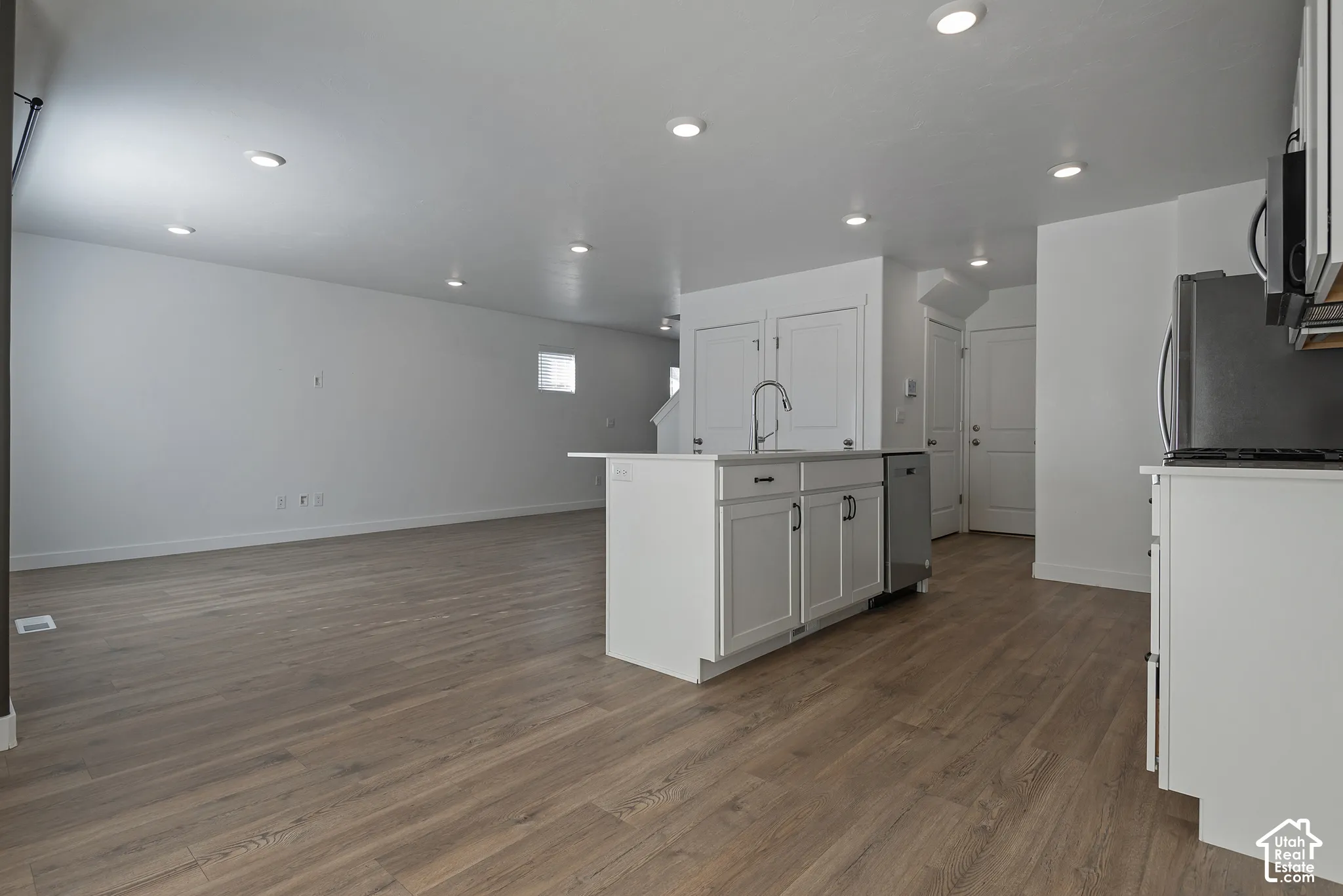 Open concept kitchen featuring recessed lighting, white cabinetry, wood-finish flooring, a central island with a stainless steel faucet, and stainless steel dishwasher