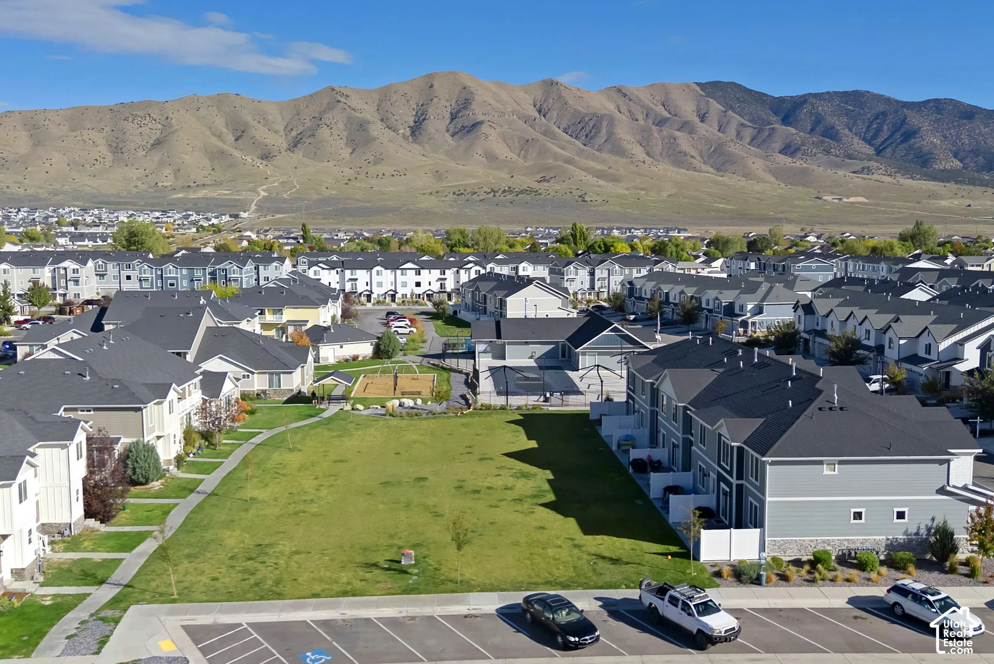 Aerial perspective of a multi-unit residential community featuring asphalt shingle roofing, exterior siding, paved surface parking, and a backdrop of mountain terrain