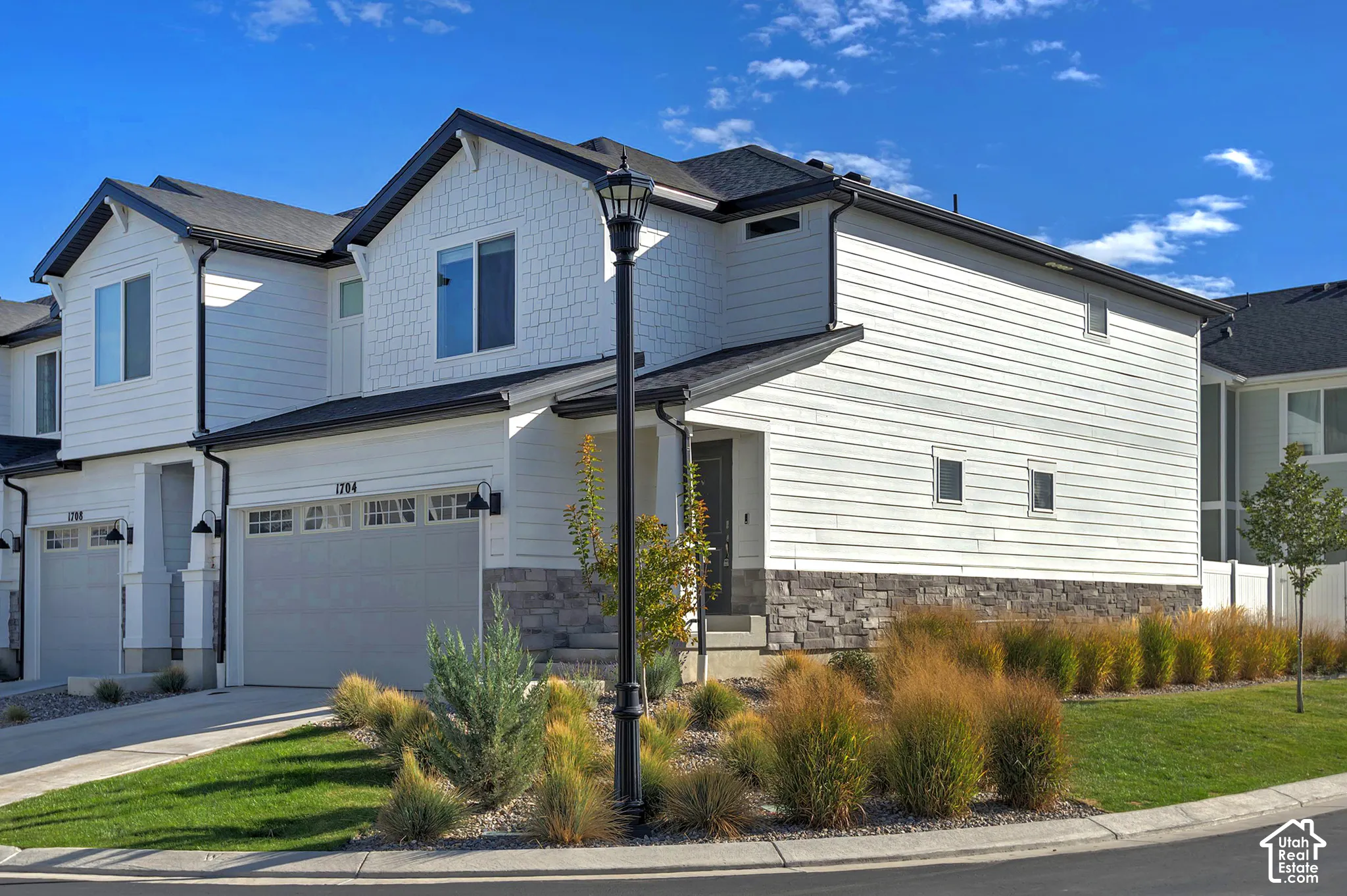 Two-story exterior featuring white horizontal siding, textured shingle accents, stone veneer foundation, multi-gabled roofline, and attached garage