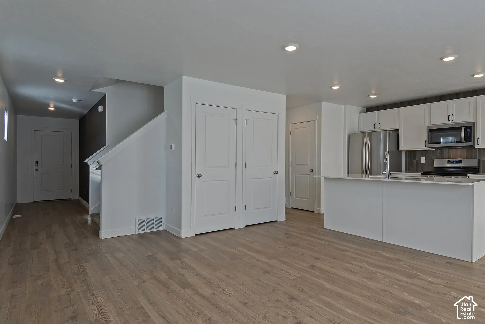 Open-concept interior featuring wood-finish flooring, white cabinetry, a kitchen island with a stone-finish countertop, recessed lighting, and stainless steel appliances
