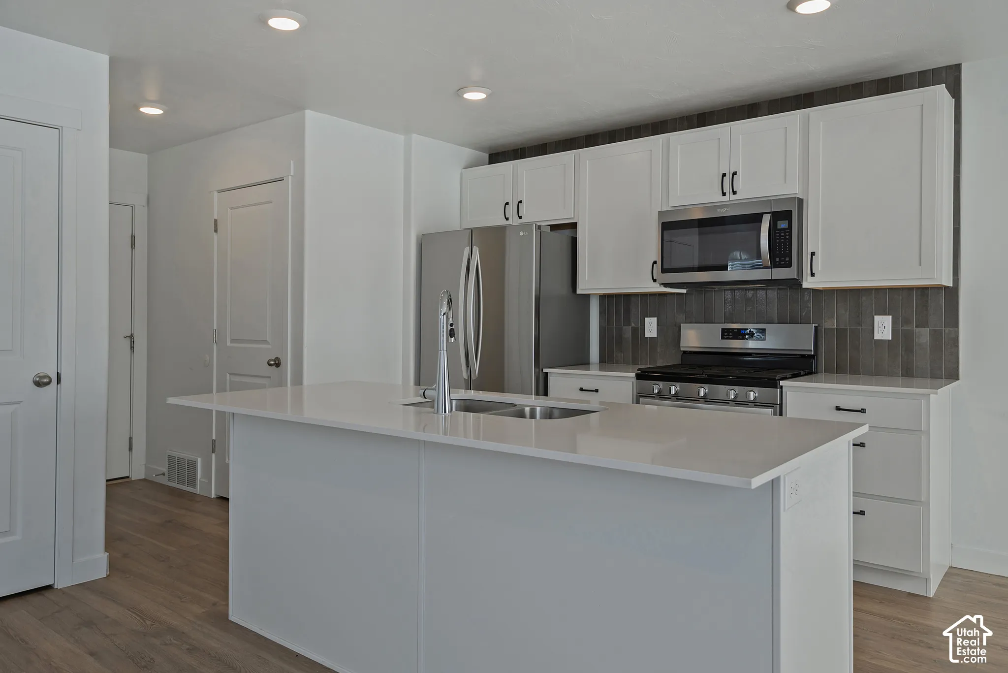 Kitchen featuring white shaker-style cabinetry, quartz countertops, a central island with a double-basin sink, stainless steel appliances, and tile backsplash