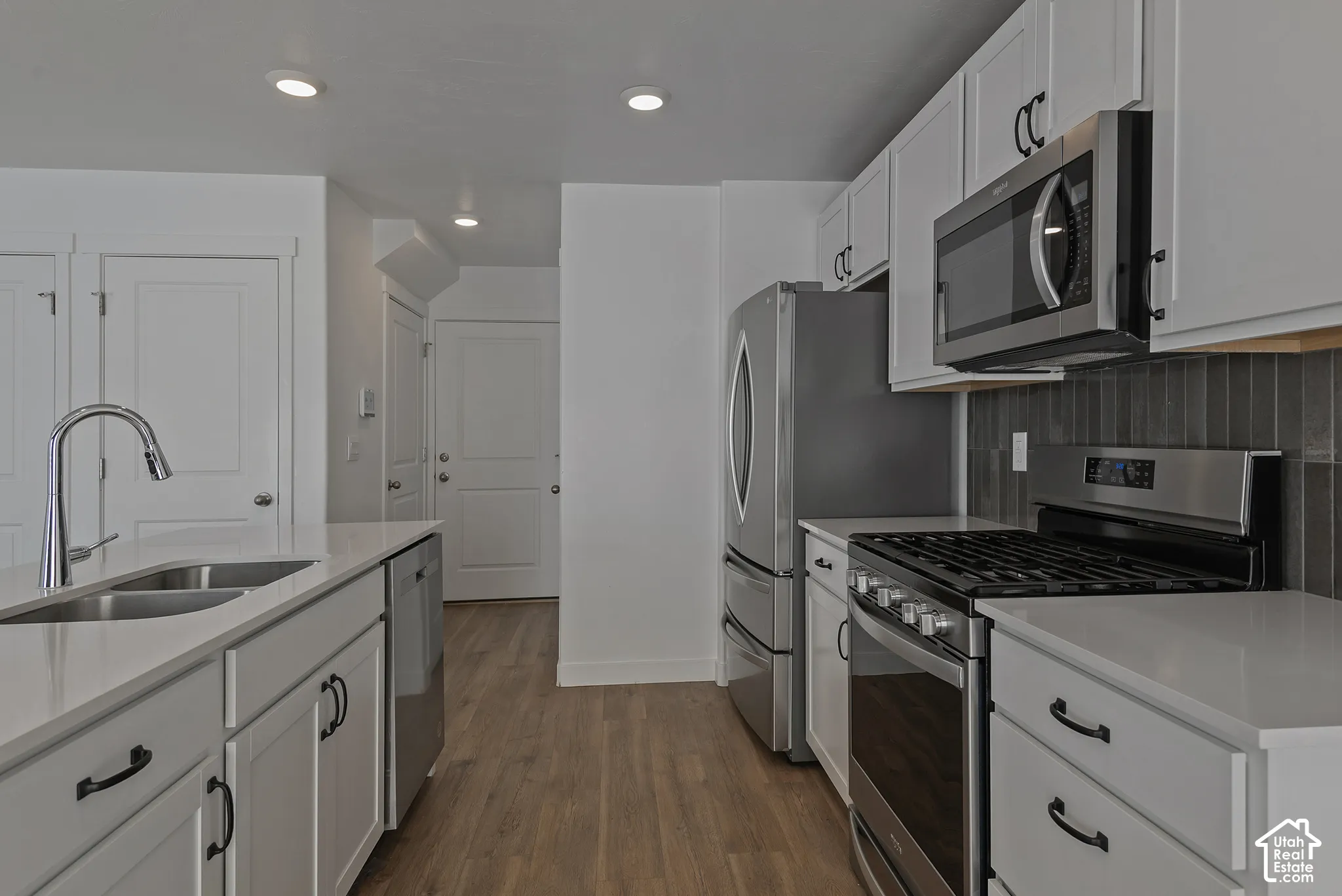 Kitchen featuring white shaker-style cabinetry, quartz countertops, stainless steel appliances, dark tile backsplash, and wood-finish flooring