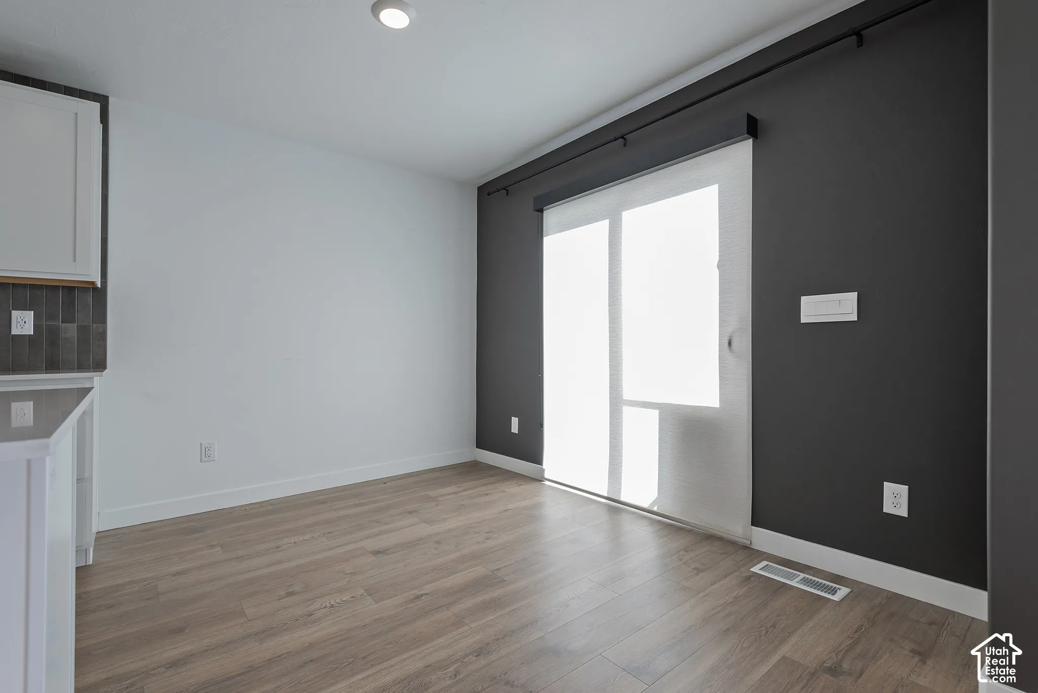Wood-finish flooring, sliding glass door with a mounted curtain rod, and contrast charcoal accent wall