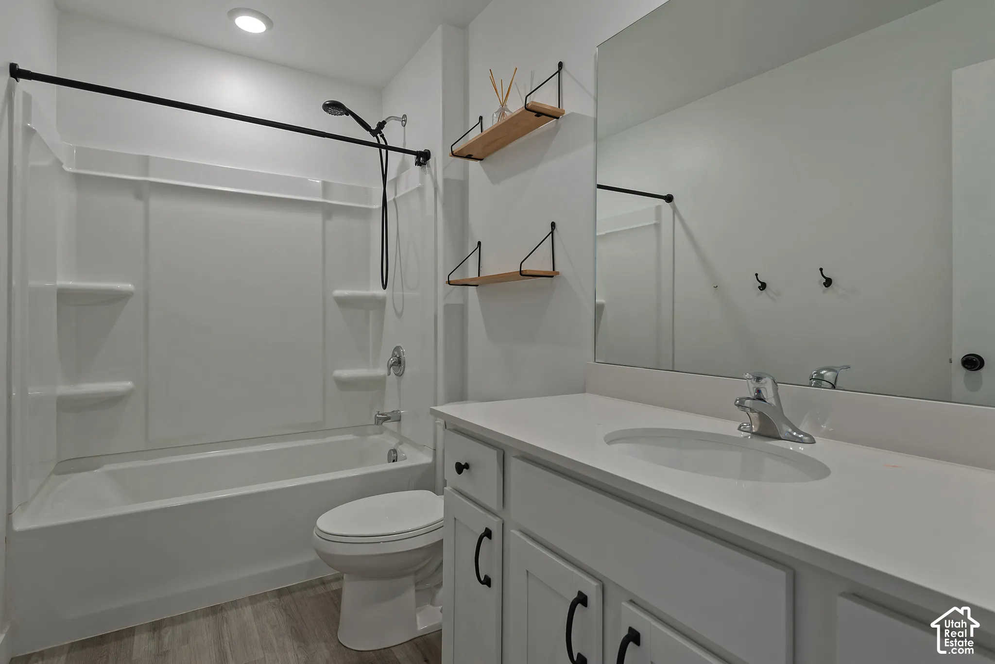 Bathroom featuring a vanity with white cabinetry and a solid-surface countertop, an oval undermount sink, a large wall-mounted mirror, and a tub-shower combination with a matte black shower head and curtain rod