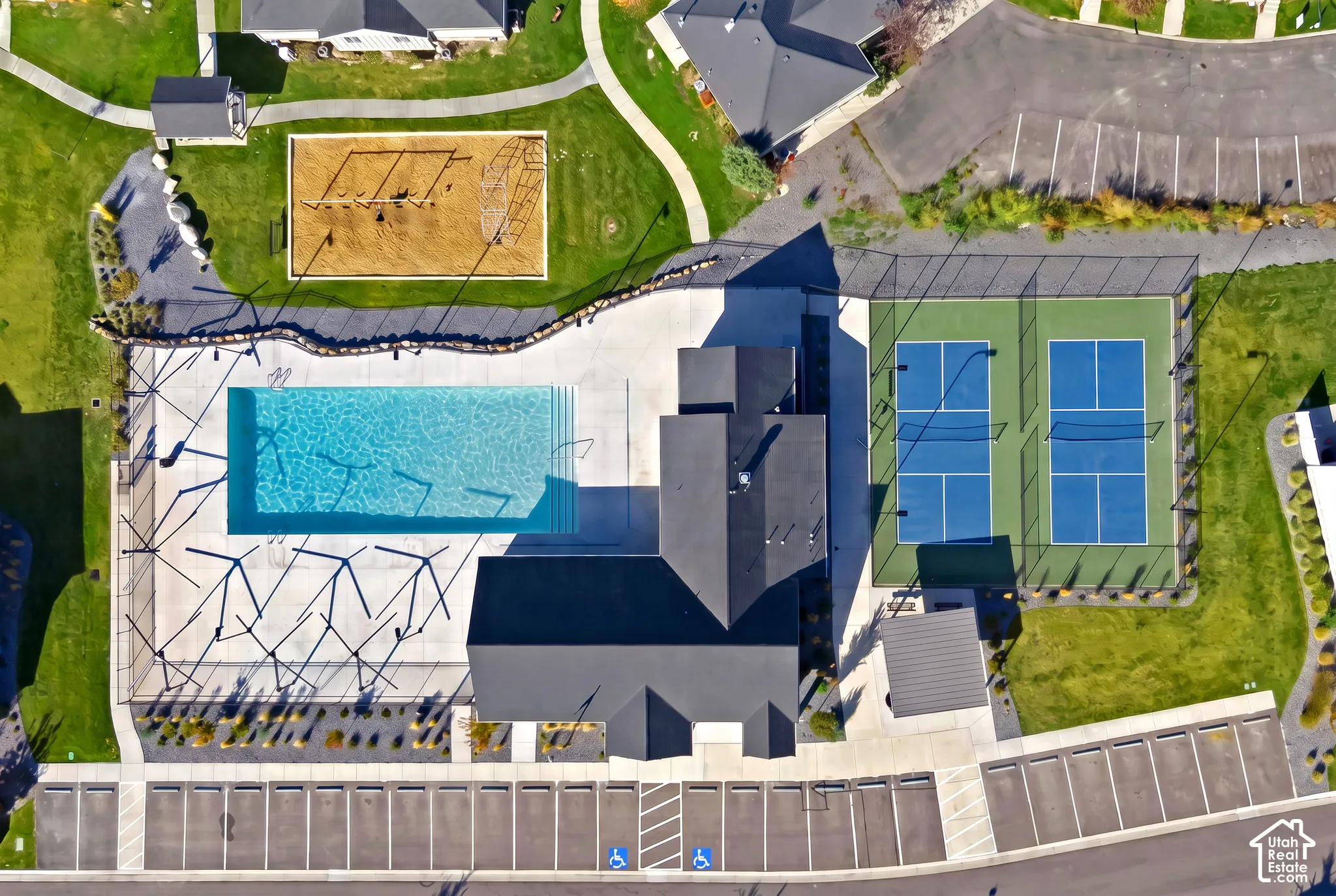 Community recreation center featuring an outdoor swimming pool, two fenced sports courts, a playground, and dedicated parking areas