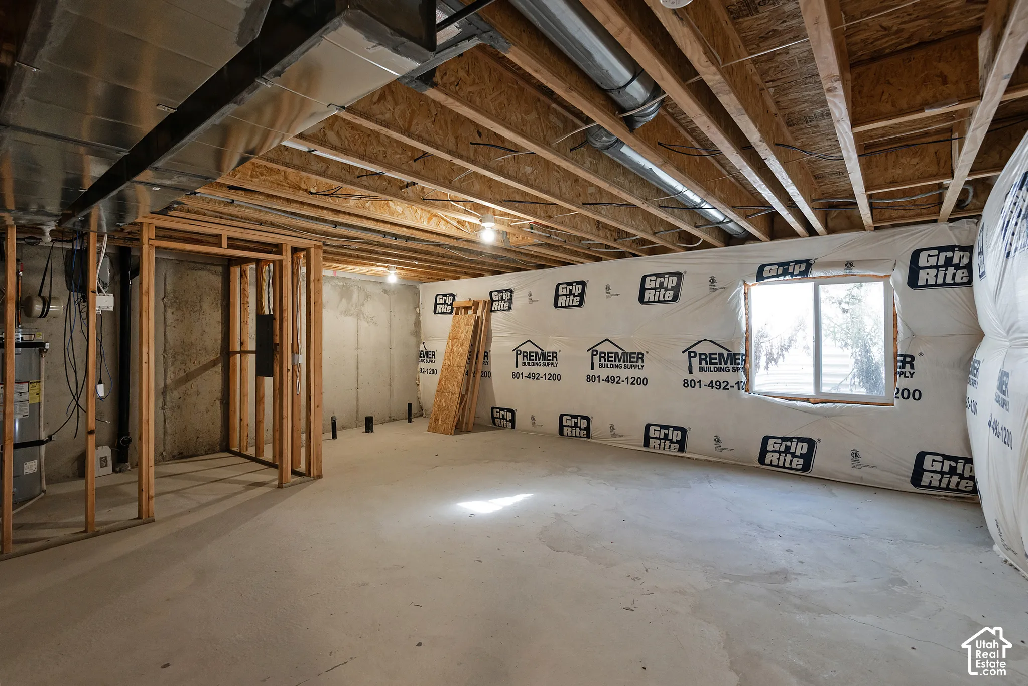 Unfinished lower level featuring concrete flooring, exposed wooden ceiling joists, metal HVAC ducting, wrapped insulation, and a single-pane window