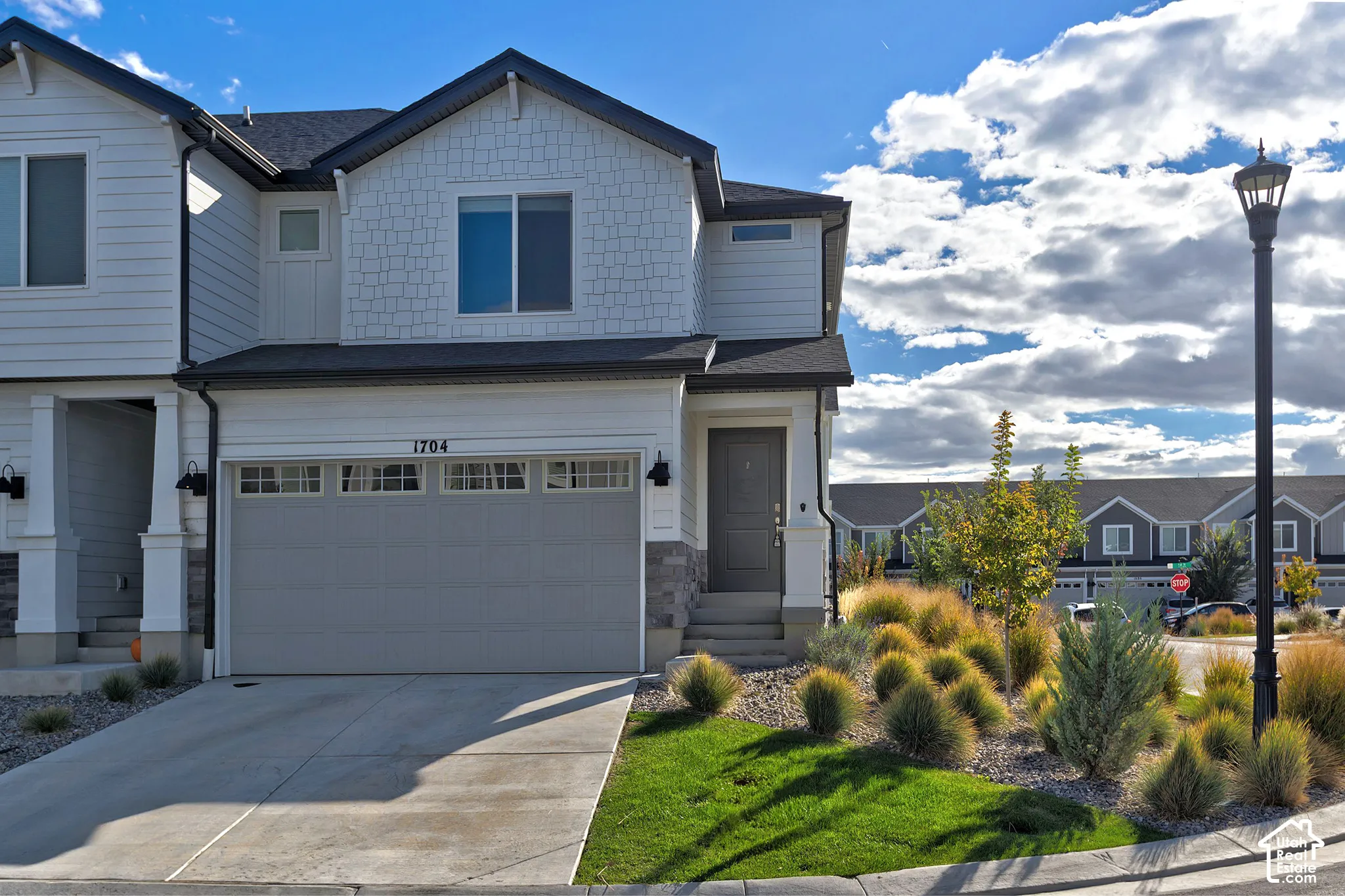 Multi-level exterior featuring white siding, stone veneer accents, shake shingle siding, a two-car garage, and professional xeriscape landscaping