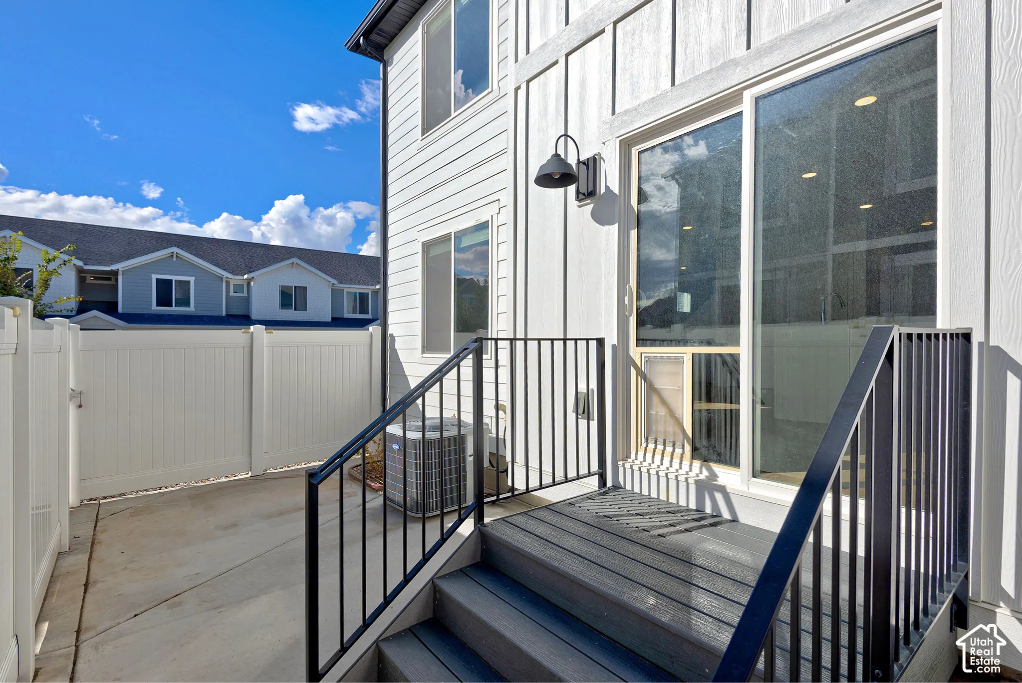Vertical board-and-batten siding exterior featuring a concrete patio, composite stair treads, black metal railings, and a wall-mounted farmhouse-style light fixture