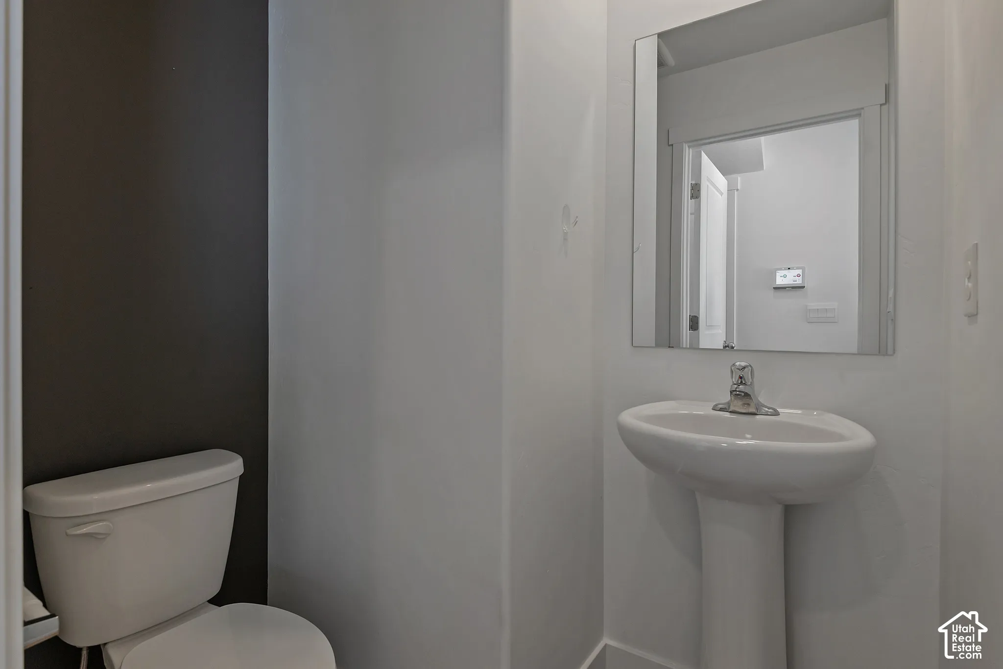 Pedestal sink with a single-lever chrome faucet, wall-mounted mirror, and an accent wall