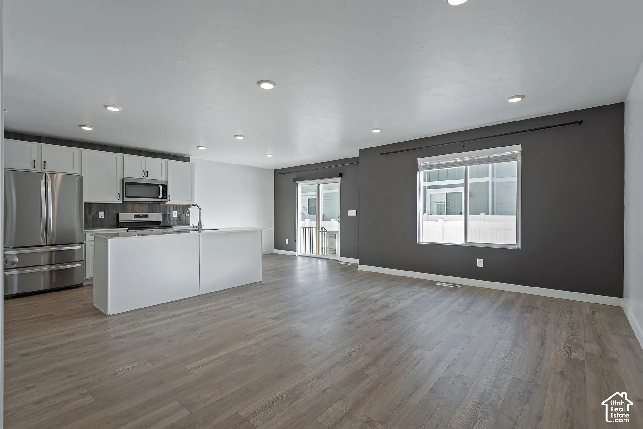 Open-concept kitchen featuring white cabinetry, stainless steel appliances, a kitchen island, recessed lighting, and wood-finish flooring