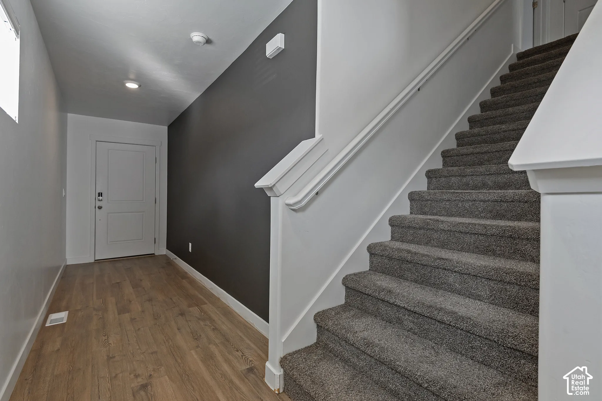 Entryway featuring wood-finish flooring, a paneled door, a dark accent wall, and a staircase with carpeted treads and a white wooden handrail