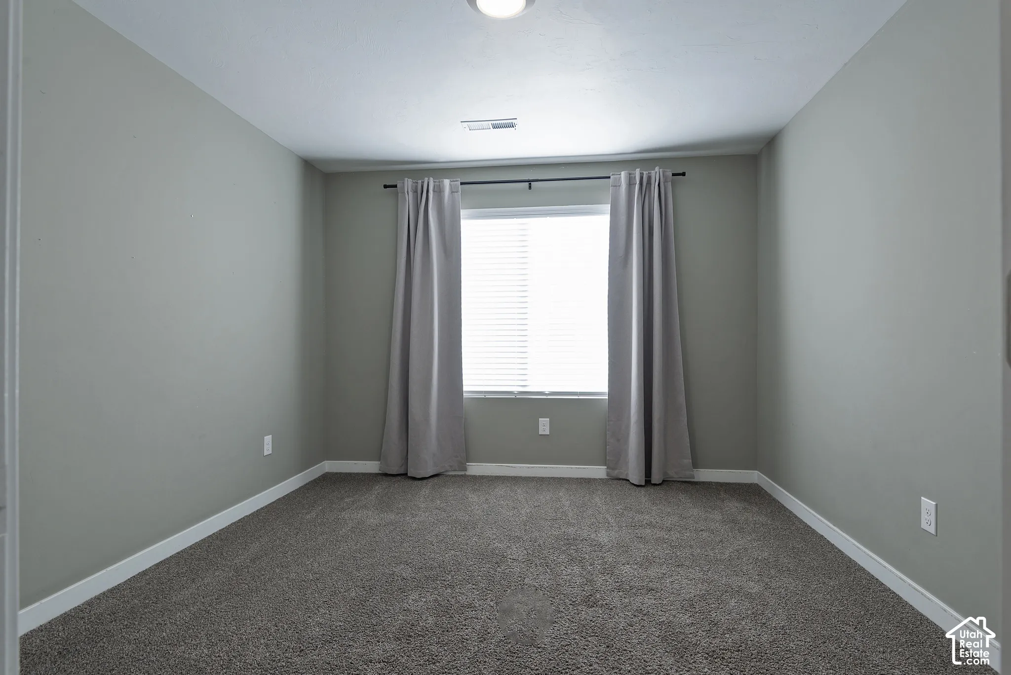 Neutral-toned interior space featuring carpeted flooring and a central window with installed horizontal blinds
