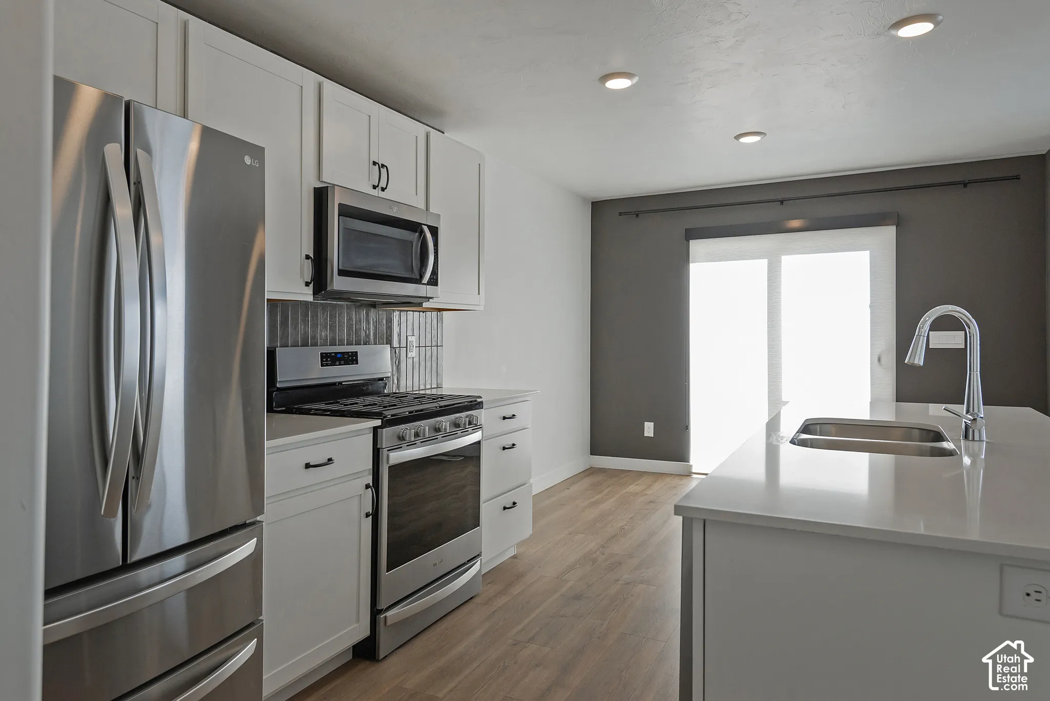 Kitchen featuring white shaker cabinetry, stainless steel appliances, quartz countertops, a central island with a stainless steel undermount sink, and wood-finish flooring