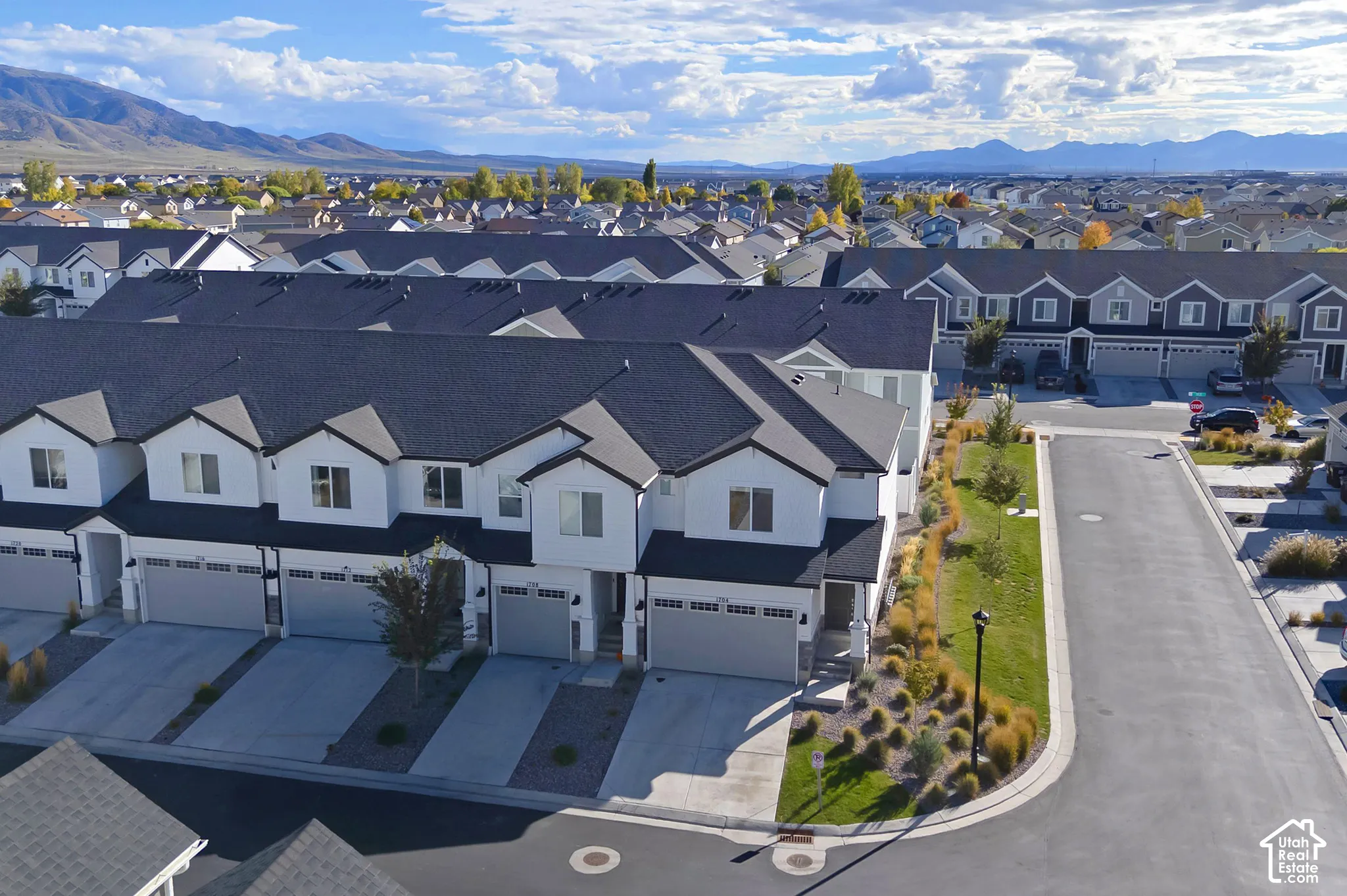 Multi-story townhome complex featuring a white exterior, multi-gabled roofline, attached multi-car garages, and concrete driveways, set against a mountainous backdrop