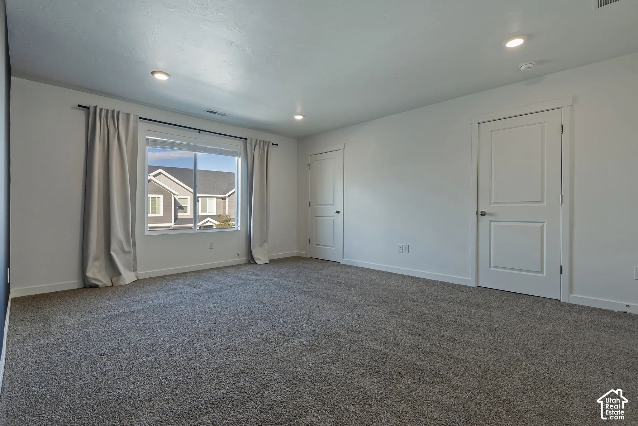 Room with neutral-toned carpeting, recessed ceiling lighting, sliding window, and two paneled doors