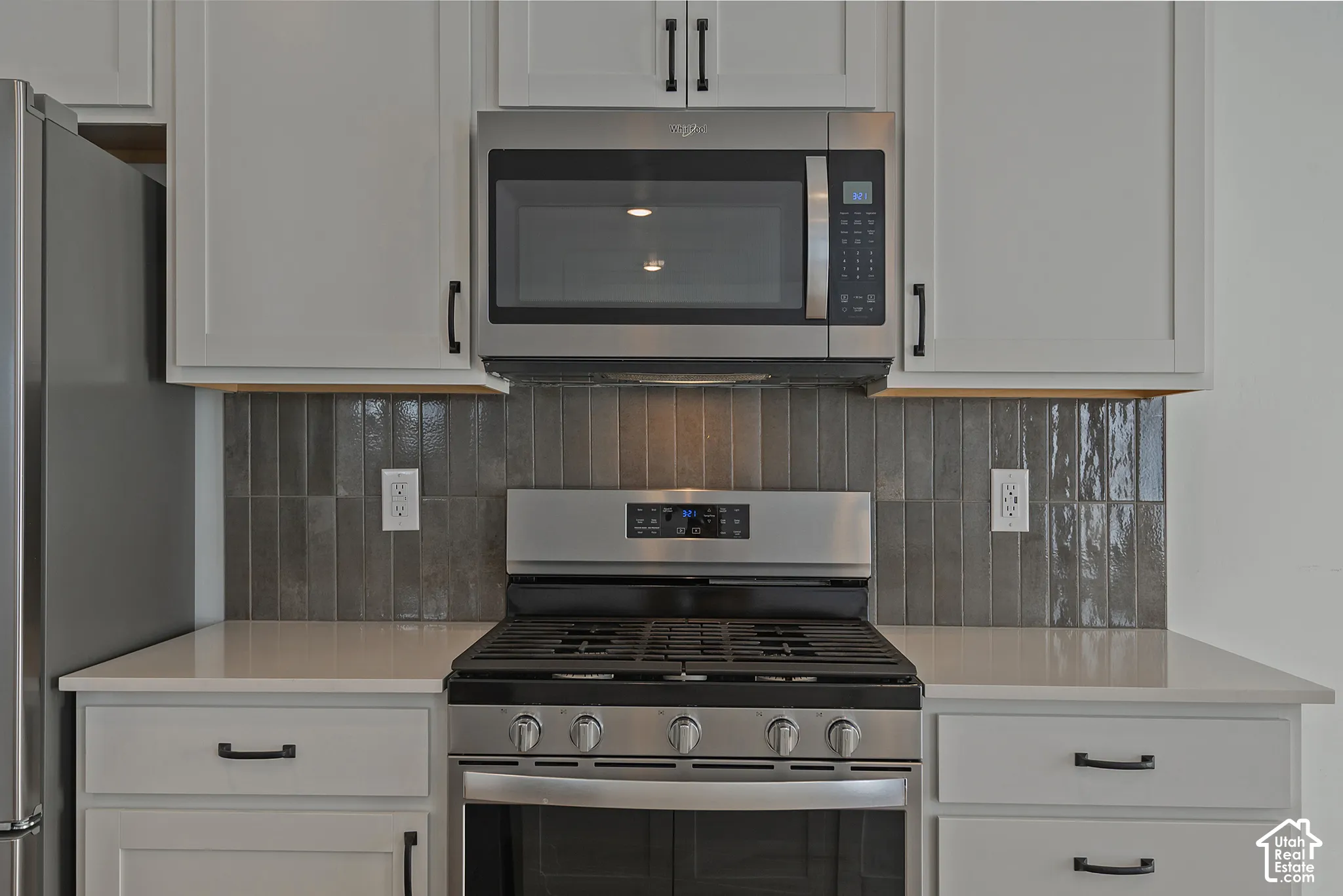 Shaker-style white cabinetry with matte black hardware, stainless steel gas range, over-the-range microwave, solid-surface countertops, and vertical subway tile backsplash