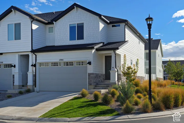 Two-story exterior featuring white horizontal siding, shake-style accents, stone veneer foundation, attached two-car garage, and a covered front entry