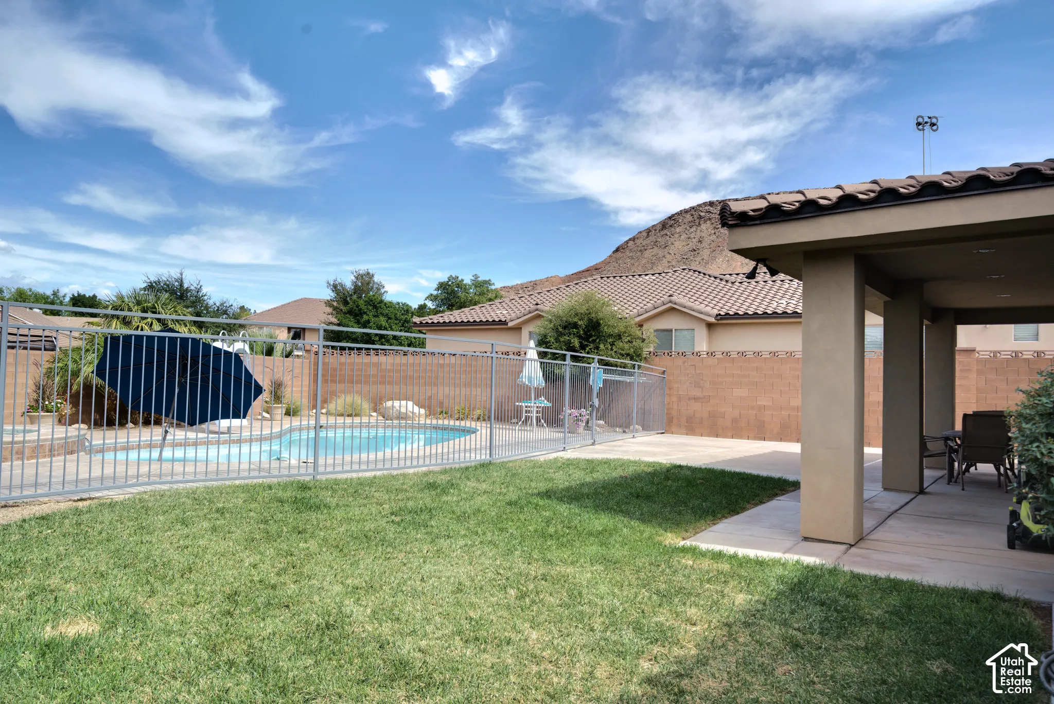 Backyard lawn, fenced pool and covered patio, with red rock behind.