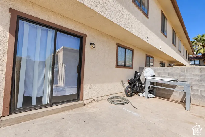 Stucco exterior featuring sliding glass doors, concrete patio, and a concrete masonry unit privacy wall