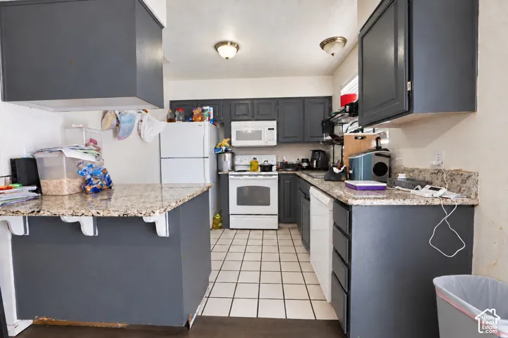 Kitchen featuring dark cabinetry, stone-surface countertops, tile flooring, and white built-in appliances