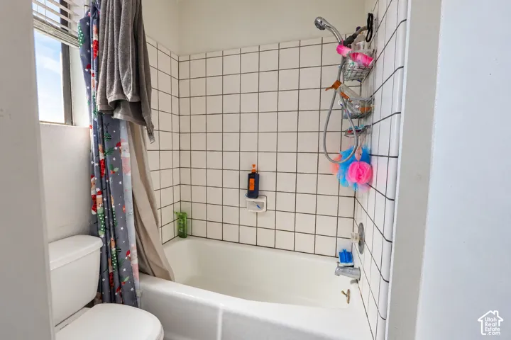 Bathroom featuring a white bathtub, white square wall tile with dark grout, a handheld shower fixture, and a window