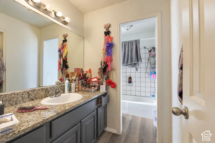 Bathroom featuring a vanity with stone-finish countertop, undermount sink, dark-toned cabinetry, full-width mirror with four-light fixture, and wood-finish flooring