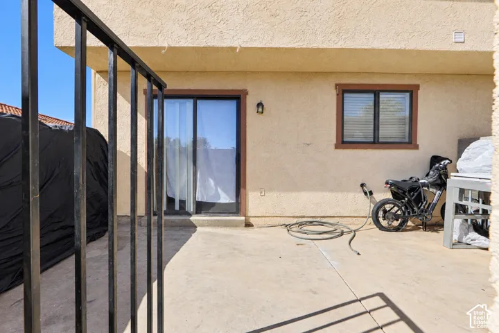 Stucco exterior featuring a concrete patio, sliding glass door, and exterior wall-mounted lighting