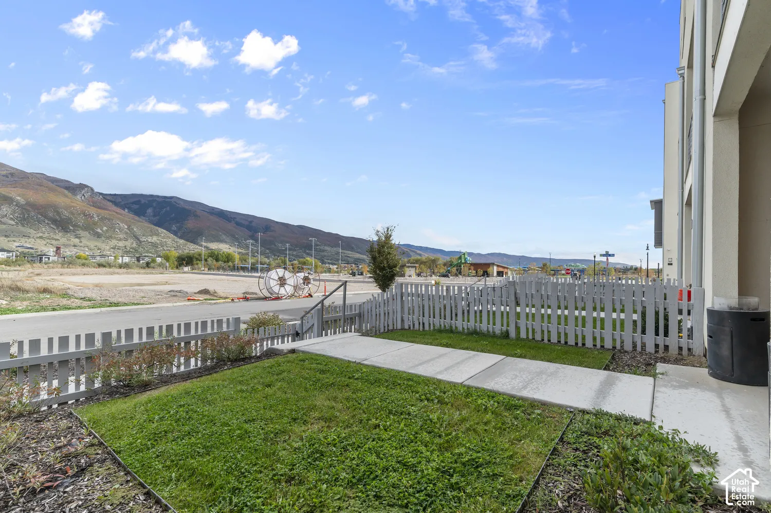 Exterior grounds featuring a concrete walkway, lawn space, and white picket fencing, set against a mountainous backdrop