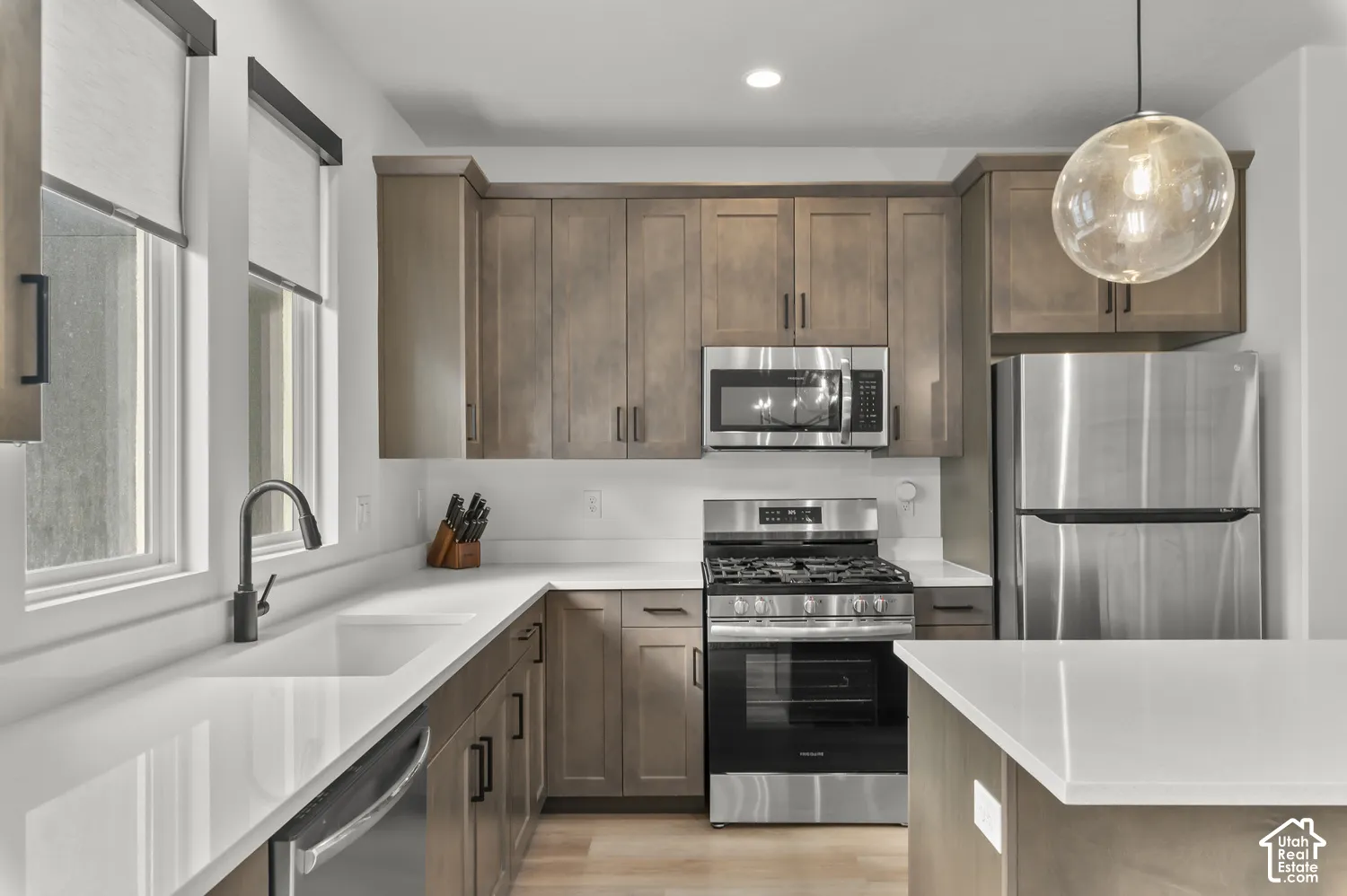 Kitchen featuring stained wood cabinetry, white stone-finish countertops, stainless steel appliances, a single-basin sink with matte black faucet, and a spherical glass pendant light