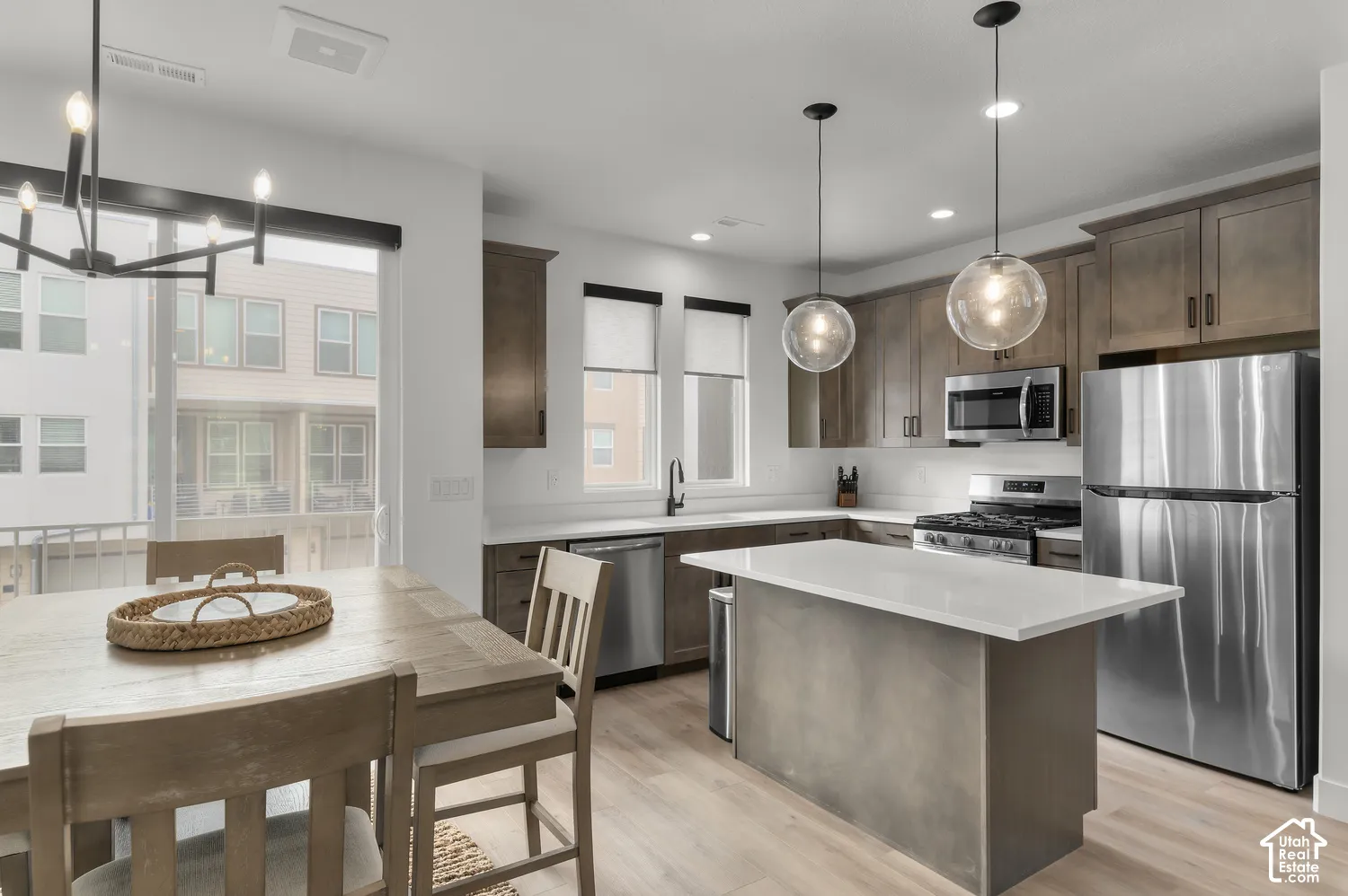 Kitchen featuring flat-panel wood-finish cabinetry, stone-surface island countertop, stainless steel appliances, and pendant lighting