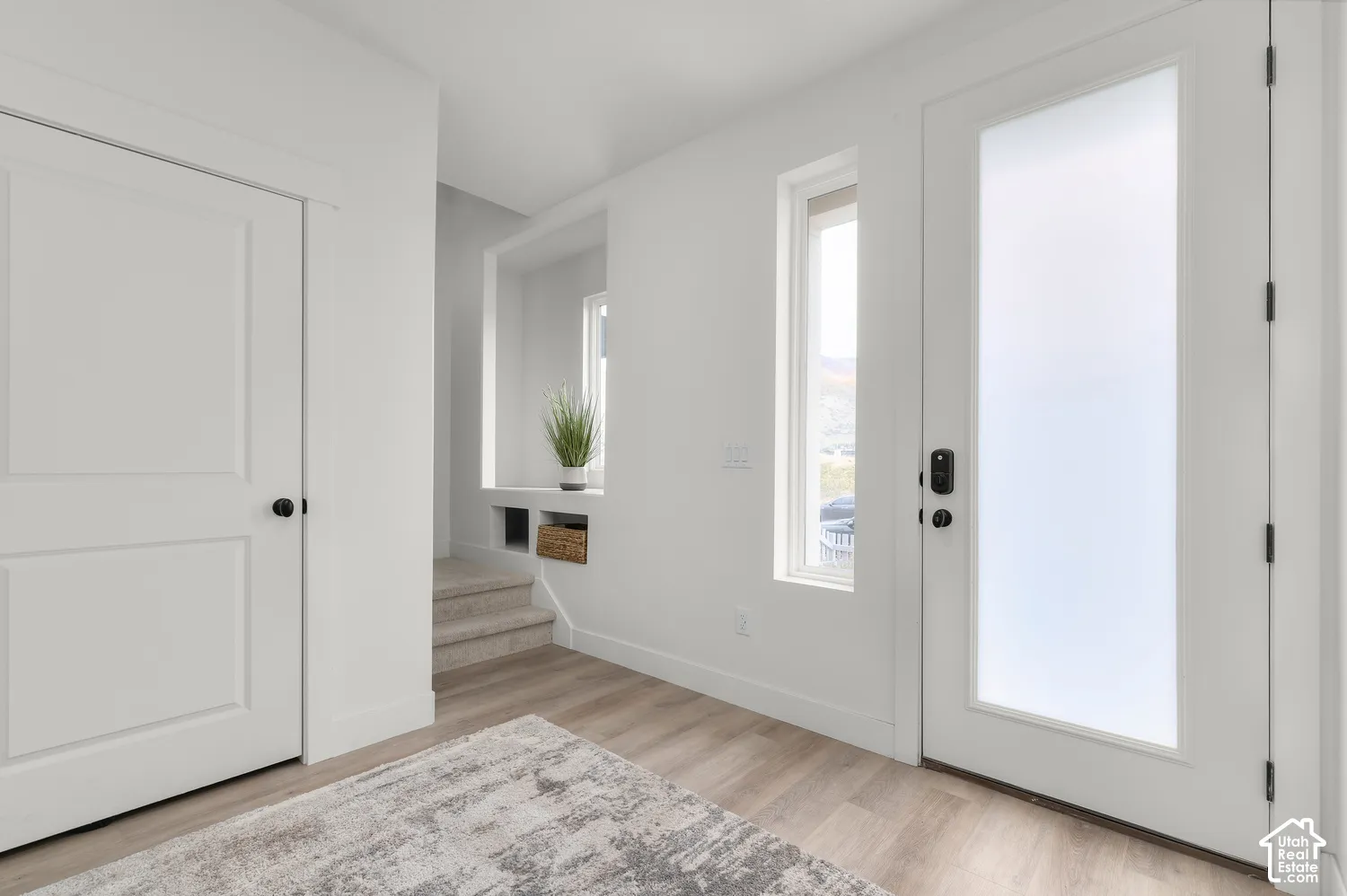 Entry featuring a door with a vertical frosted glass insert, wood-finish flooring, a built-in recessed wall niche, and tall rectangular windows