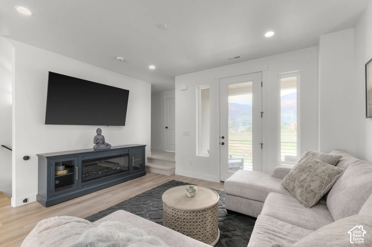 Living area featuring wood-finish flooring, recessed lighting, and a glass-paneled exterior door flanked by two side windows