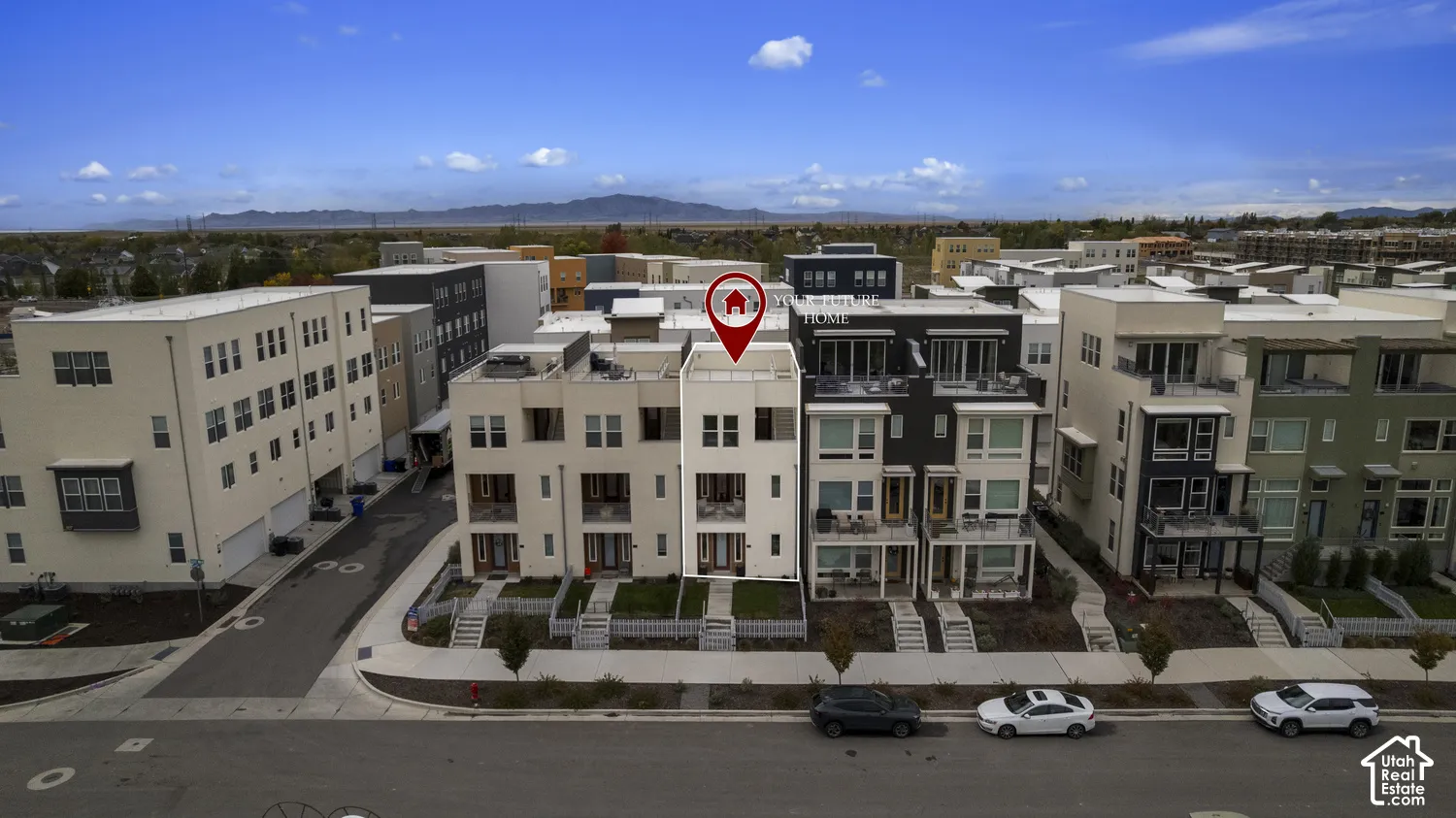Multi-story townhome exterior featuring a rooftop terrace, private balconies, light-toned masonry facade, and mountain backdrops