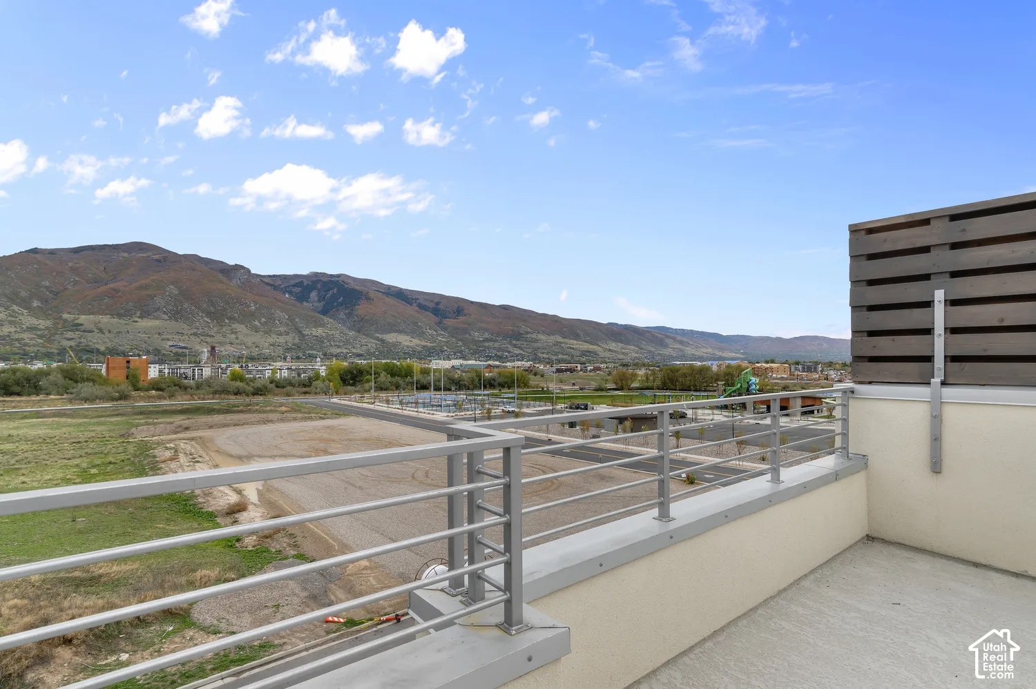 Outdoor balcony featuring metal railing, horizontal wood-slat privacy screen, concrete flooring, and mountainous backdrop