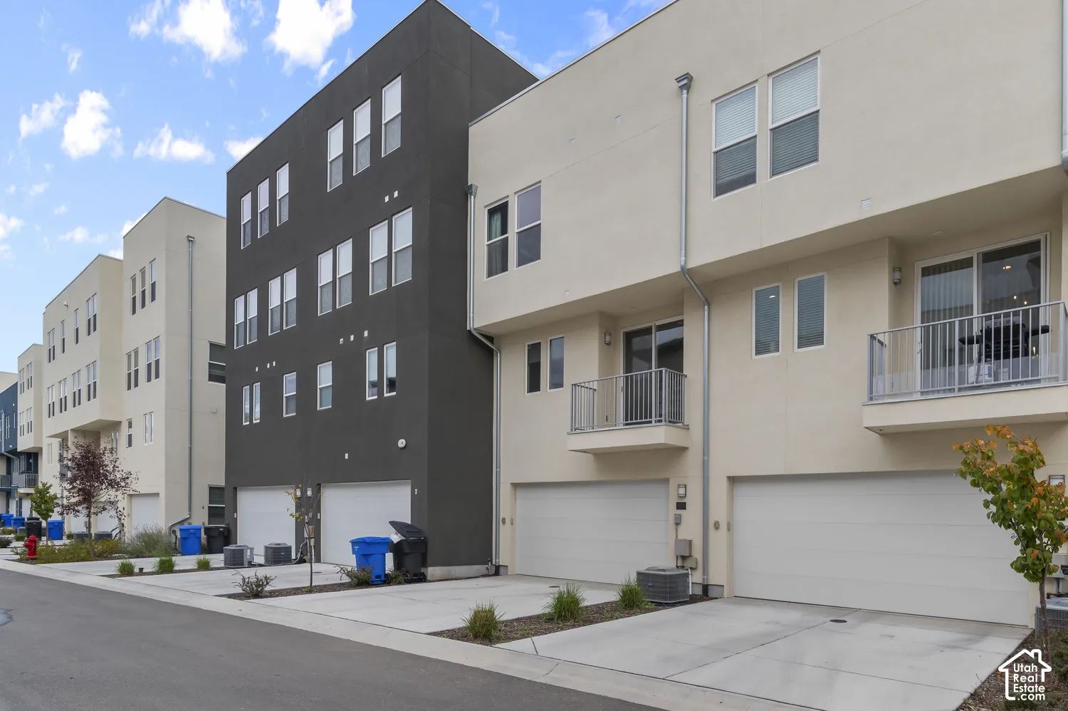Contemporary multi-story exterior featuring a high-contrast dark and light facade, private balconies with metal railings, and attached multi-car garages
