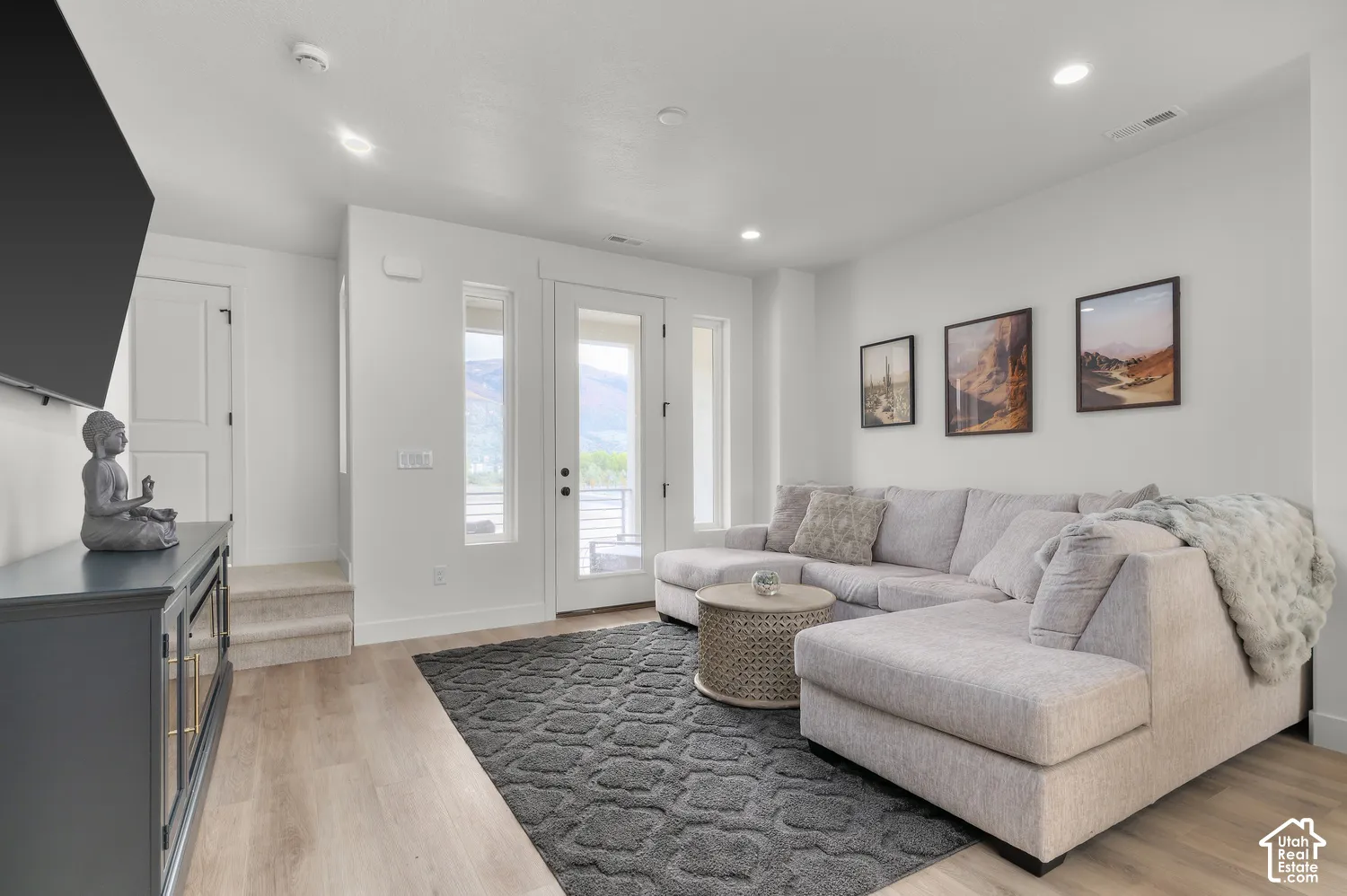 Open-concept area featuring light-toned wood-finish flooring, recessed lighting, neutral wall paint, and a glass-paneled exterior door flanked by vertical windows