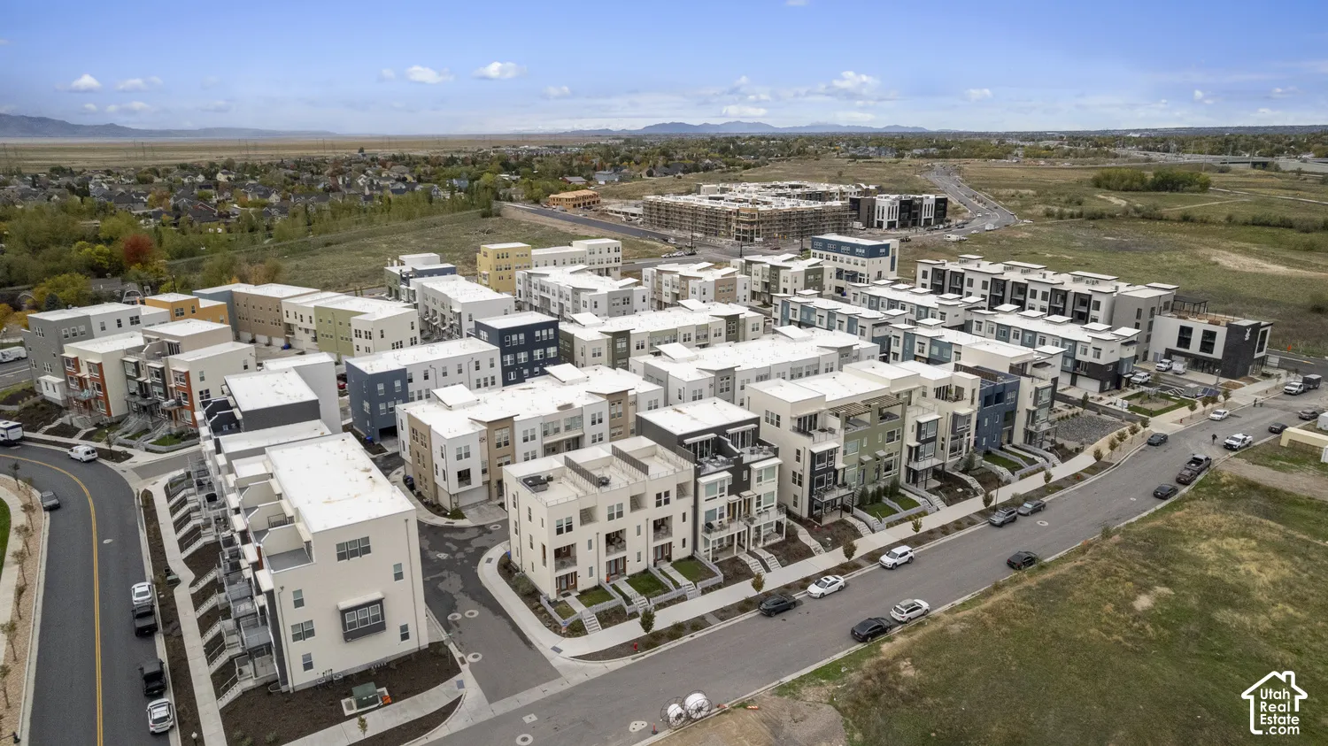 Aerial perspective of a multi-unit residential complex featuring contemporary stucco exteriors, integrated balconies, paved street access, and surrounding open terrain