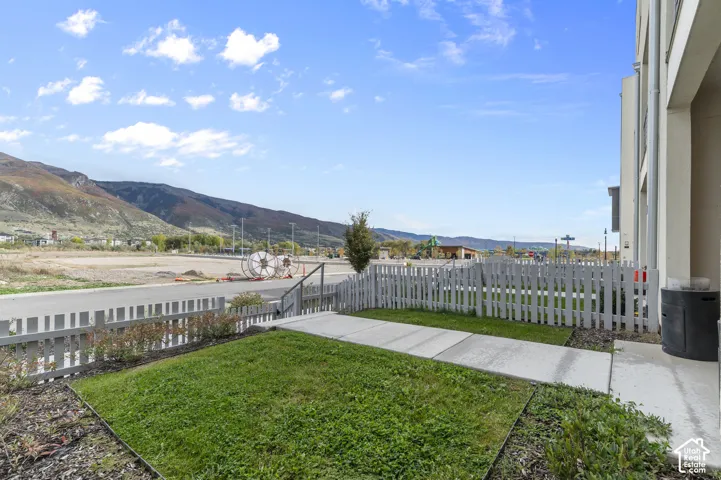 Exterior grounds featuring a concrete walkway, lawn space, and white picket fencing, set against a mountainous backdrop