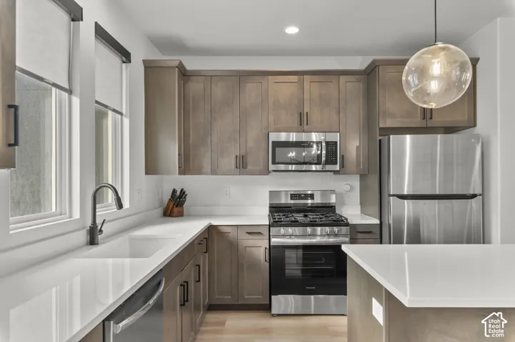 Kitchen featuring stained wood cabinetry, white stone-finish countertops, stainless steel appliances, a single-basin sink with matte black faucet, and a spherical glass pendant light