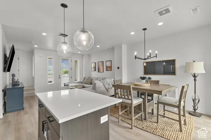 Kitchen island featuring a quartz countertop and dark cabinetry, complemented by sphere pendant lighting, recessed ceiling lights, and light-tone wood-finish flooring