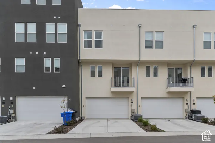 Contemporary exterior featuring a mix of charcoal and cream stucco, multi-level design, individual attached garages, and private second-story balconies with metal railings