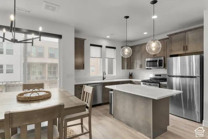 Kitchen featuring flat-panel wood-finish cabinetry, stone-surface island countertop, stainless steel appliances, and pendant lighting