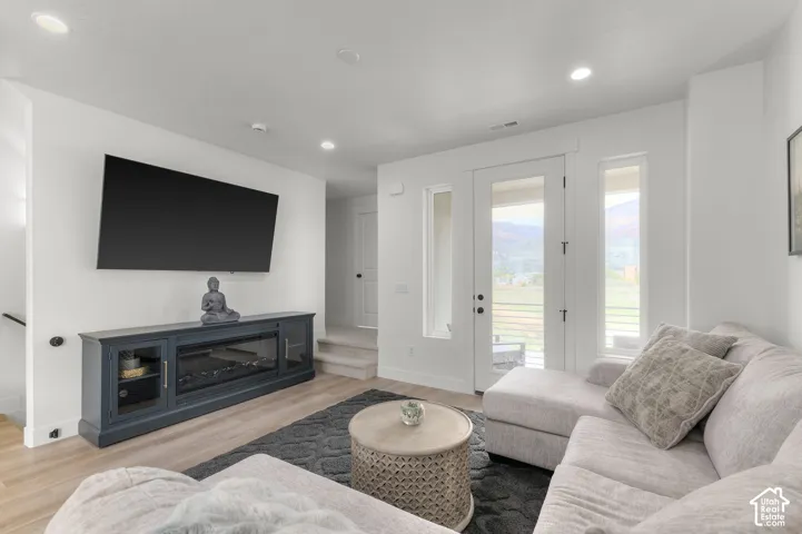 Living area featuring wood-finish flooring, recessed lighting, and a glass-paneled exterior door flanked by two side windows