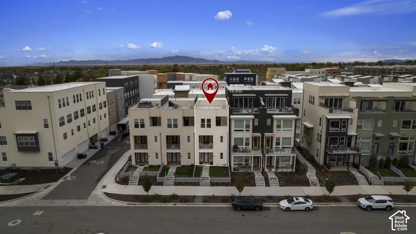 Multi-story townhome exterior featuring a rooftop terrace, private balconies, light-toned masonry facade, and mountain backdrops