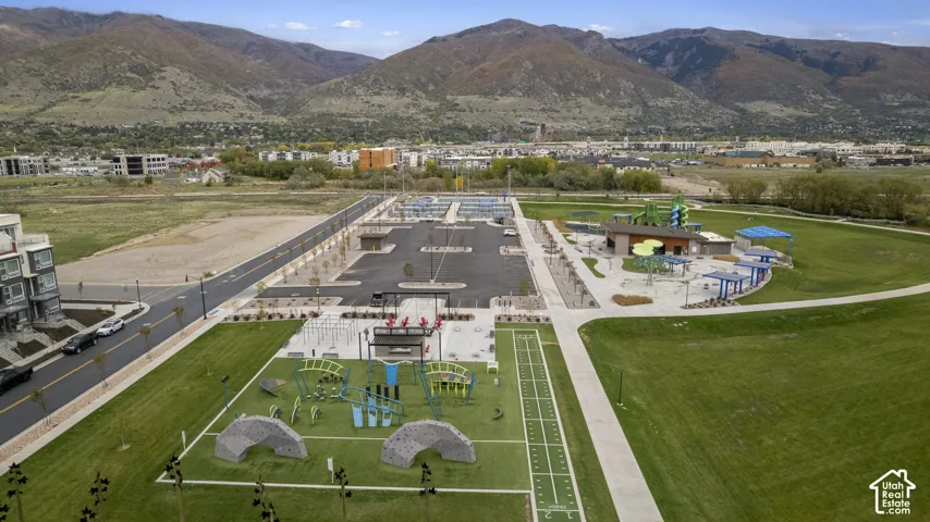 Expansive outdoor recreational area featuring a paved multi-use court, climbing structures, synthetic turf surfacing, and pedestrian pathways set against a mountain backdrop