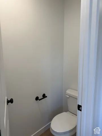 Commode area featuring a white toilet, matte black toilet paper holder, and matte black door hardware