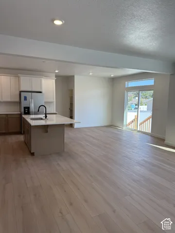 Kitchen featuring wood-finish flooring, white upper cabinetry, a central island with a stone-composite countertop, matte black faucet, and sliding glass doors with a transom window