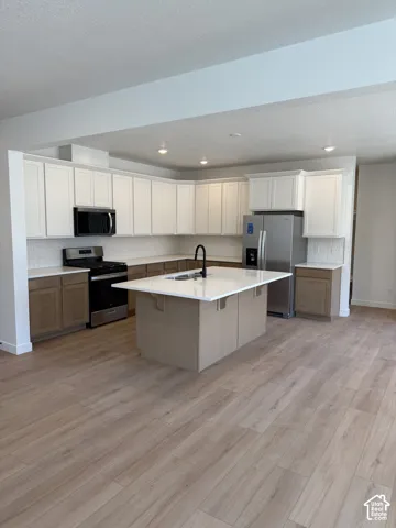 Kitchen featuring two-tone cabinetry, central island with a quartz countertop, white tile backsplash, stainless steel appliances, and wood-finish flooring