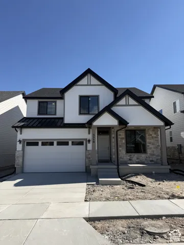Two-story exterior featuring a mix of stone veneer and board-and-batten siding, a metal roof accent over the garage, a covered front porch with concrete steps, and a multi-panel sectional garage door