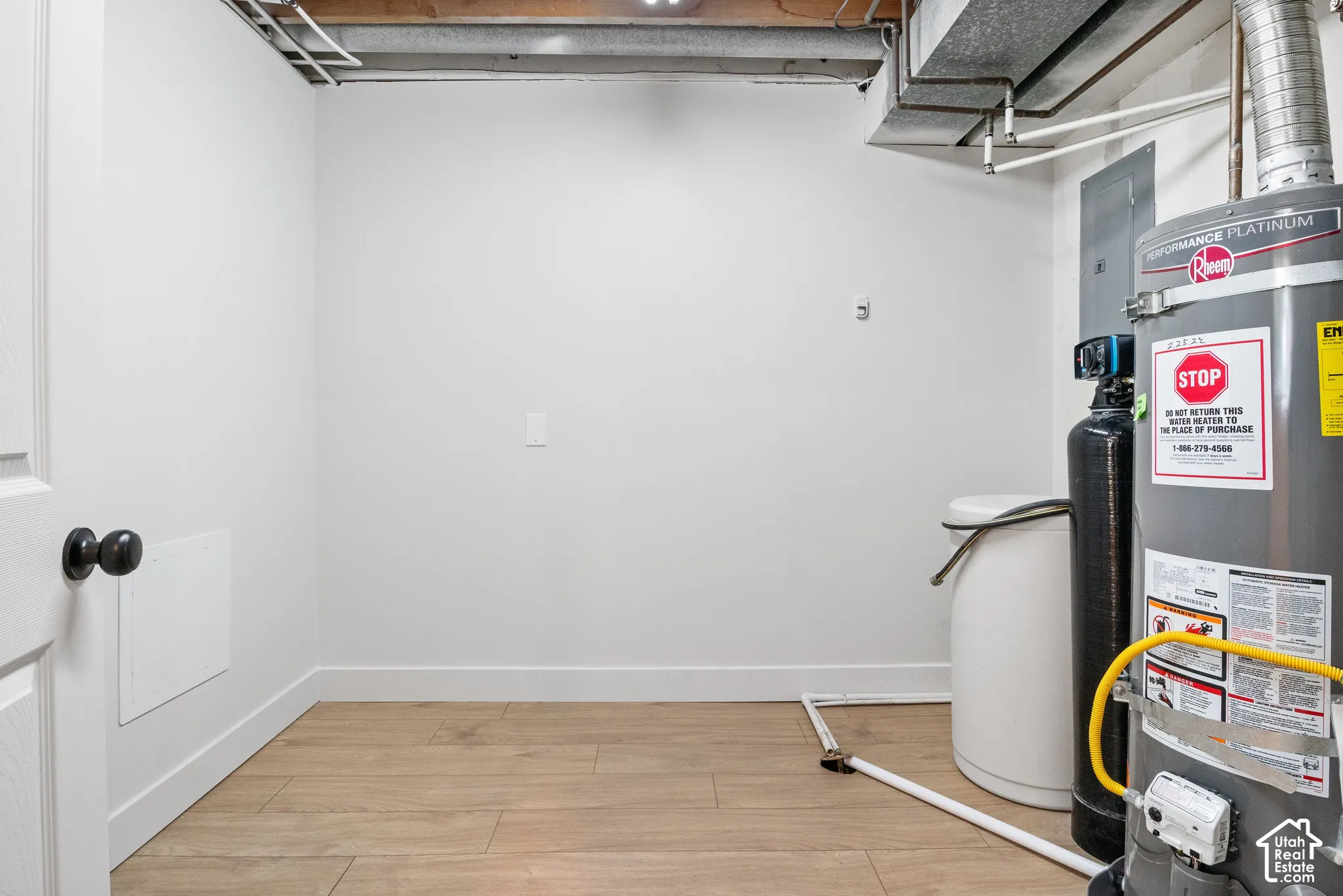 Utility space featuring wood-finish flooring, a water heater, a water softener system, and an electrical panel